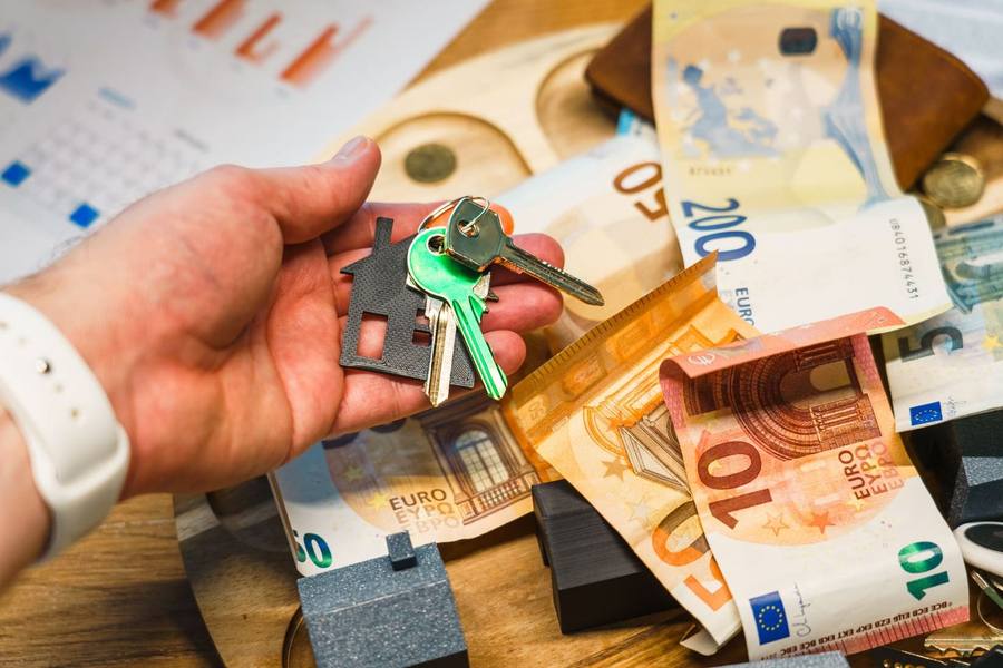 Trousseau de clés à porte-clés en forme de maison posé sur des billets